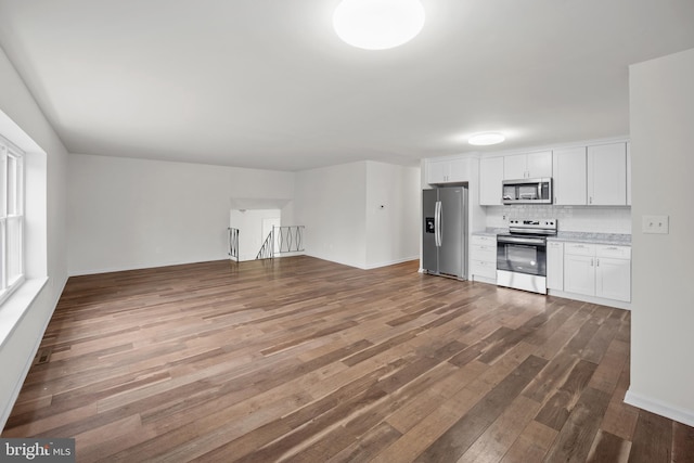 kitchen featuring tasteful backsplash, open floor plan, dark wood-type flooring, stainless steel appliances, and white cabinetry