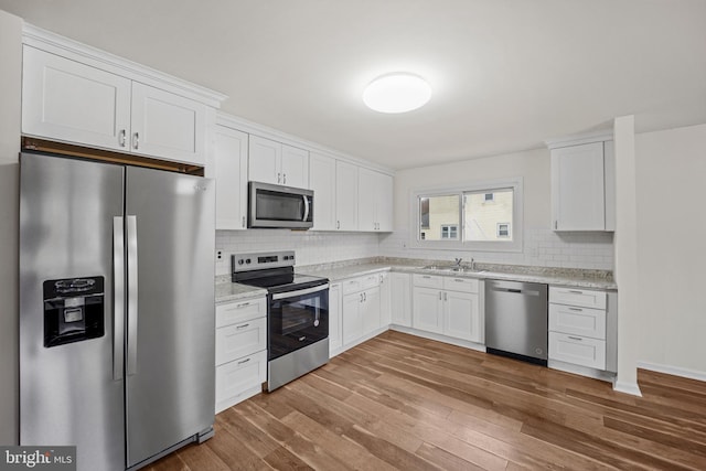 kitchen featuring wood finished floors, a sink, white cabinetry, appliances with stainless steel finishes, and backsplash