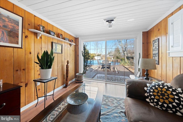 living area with crown molding, wooden walls, and wood finished floors