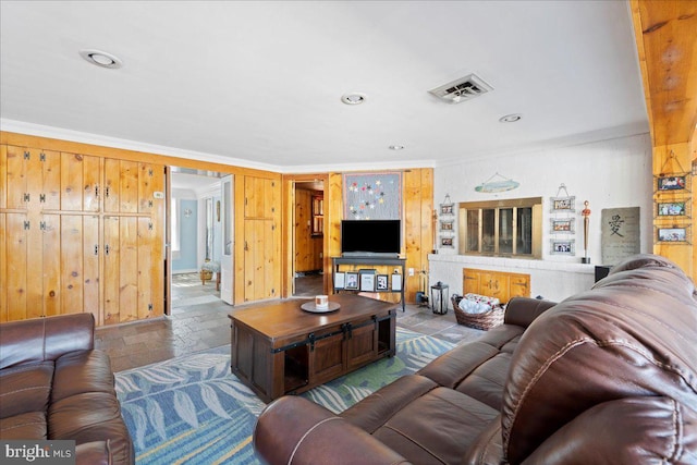 living room with crown molding, recessed lighting, visible vents, stone finish floor, and wooden walls