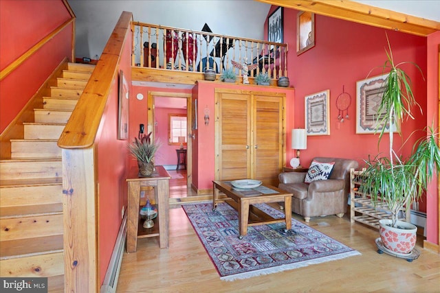 living area with stairway, baseboard heating, wood finished floors, and a towering ceiling