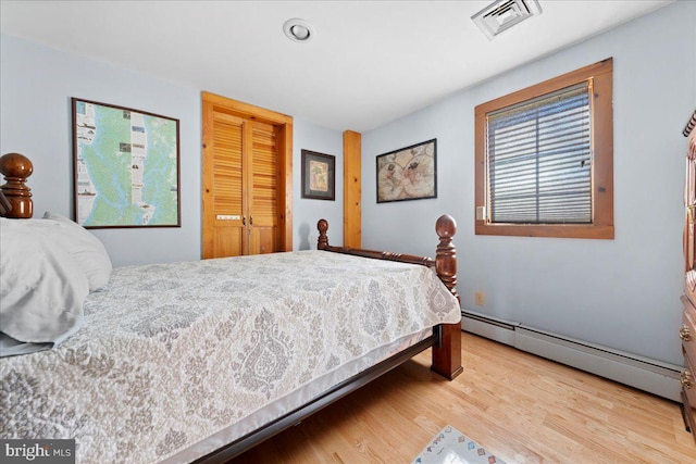 bedroom with a closet, baseboard heating, wood finished floors, and visible vents