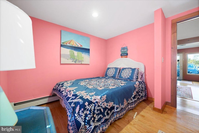 bedroom with a baseboard heating unit, wood finished floors, and baseboards