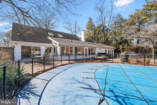 rear view of property with brick siding, a shingled roof, fence, a fenced in pool, and a chimney