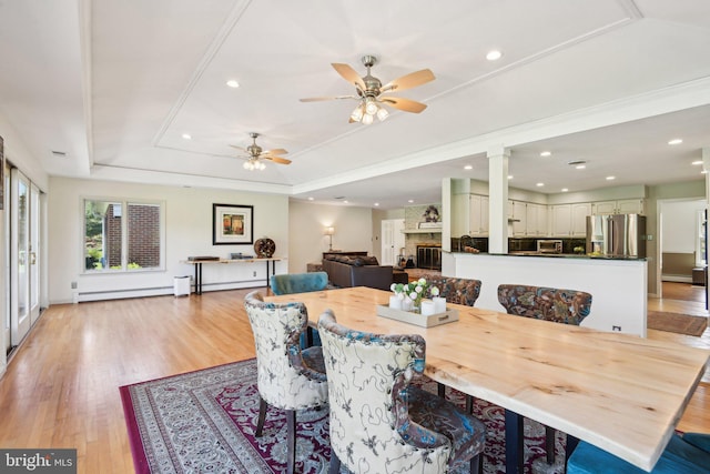 dining space with a tray ceiling, a ceiling fan, recessed lighting, baseboard heating, and light wood finished floors