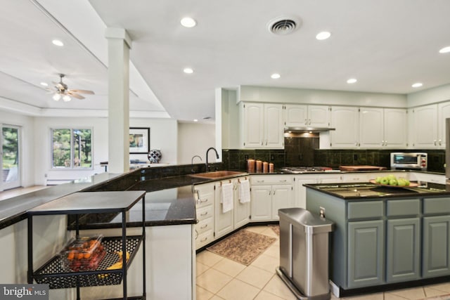 kitchen with light tile patterned floors, tasteful backsplash, a peninsula, white cabinets, and a sink
