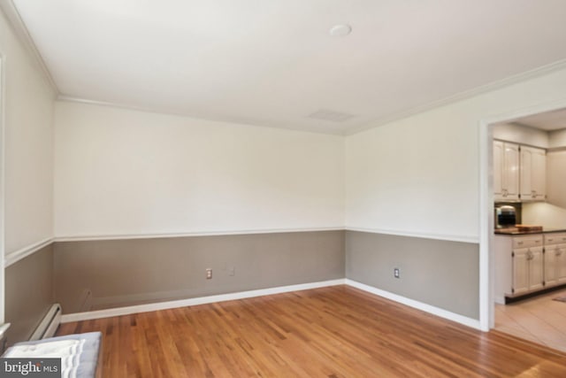 empty room with crown molding, light wood finished floors, baseboards, and a baseboard radiator
