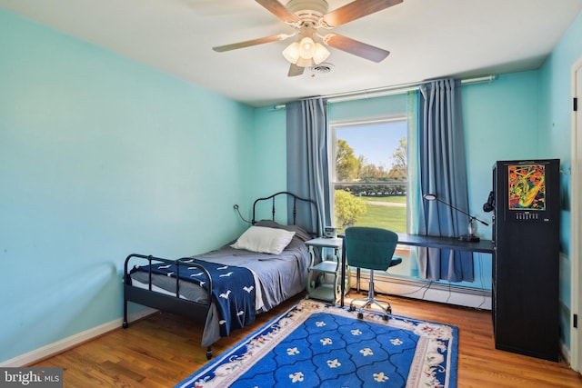 bedroom with a ceiling fan, visible vents, baseboard heating, wood finished floors, and baseboards