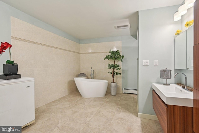 full bathroom with a freestanding tub, vanity, baseboard heating, visible vents, and tile walls