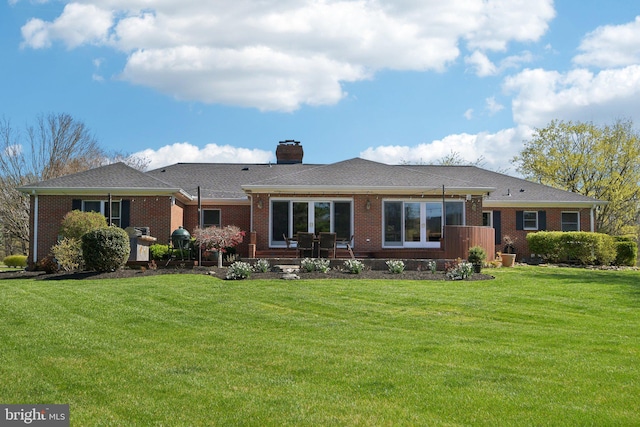 back of house with a yard, roof with shingles, brick siding, and a chimney