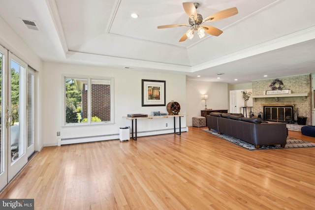 living area featuring visible vents, a tray ceiling, a ceiling fan, and light wood-style flooring