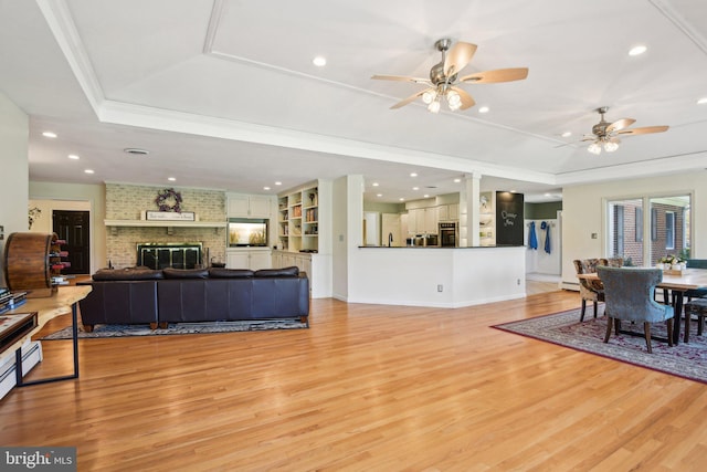 living room featuring a raised ceiling, a ceiling fan, and light wood-style flooring