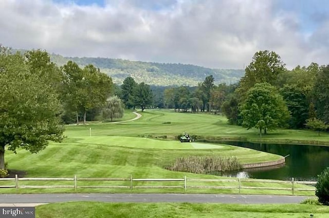 surrounding community featuring a lawn, fence, view of golf course, and a water view