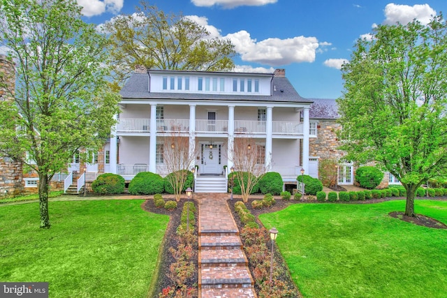 greek revival house with a front yard, a porch, and a shingled roof