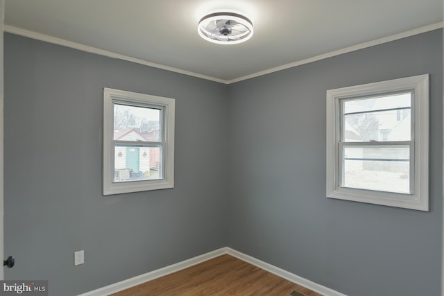 empty room featuring crown molding, baseboards, and wood finished floors