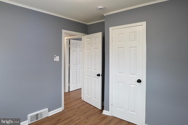 unfurnished bedroom featuring ornamental molding, visible vents, baseboards, and wood finished floors