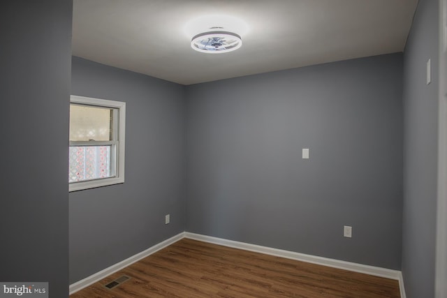 empty room with dark wood-style floors, visible vents, and baseboards