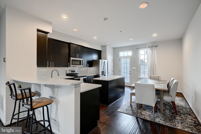 kitchen with a center island, a breakfast bar, stainless steel appliances, decorative backsplash, and dark wood-type flooring