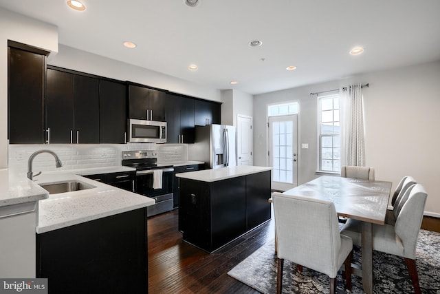 kitchen featuring tasteful backsplash, dark wood-style floors, a kitchen island, stainless steel appliances, and a sink