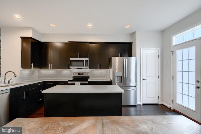 kitchen with appliances with stainless steel finishes, backsplash, a sink, and a center island