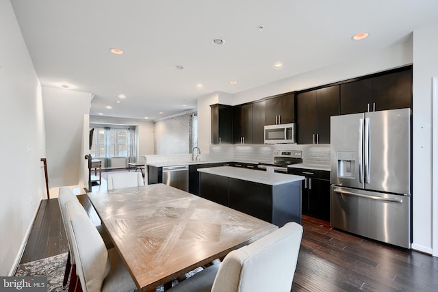 kitchen featuring dark wood-style flooring, stainless steel appliances, light countertops, backsplash, and a kitchen island