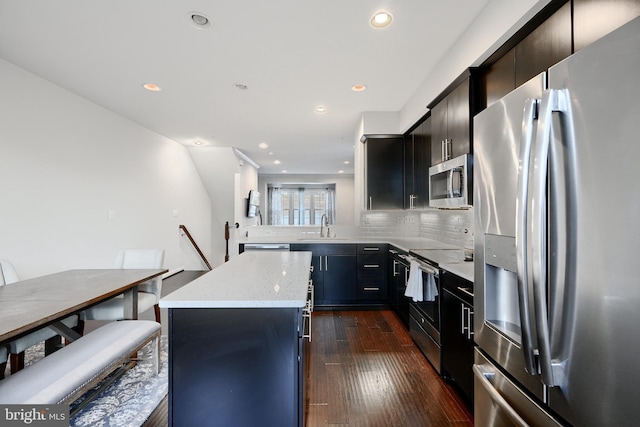 kitchen featuring dark wood finished floors, a center island, stainless steel appliances, dark cabinetry, and a sink