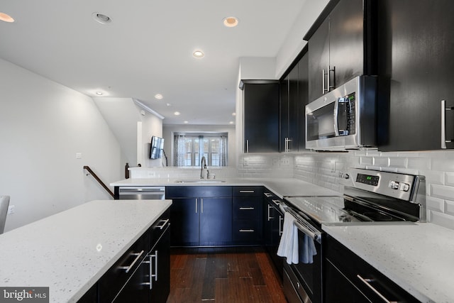 kitchen featuring tasteful backsplash, dark wood-style floors, dark cabinets, stainless steel appliances, and a sink