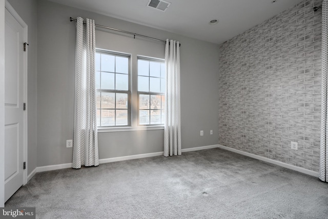 carpeted spare room featuring brick wall, visible vents, and baseboards