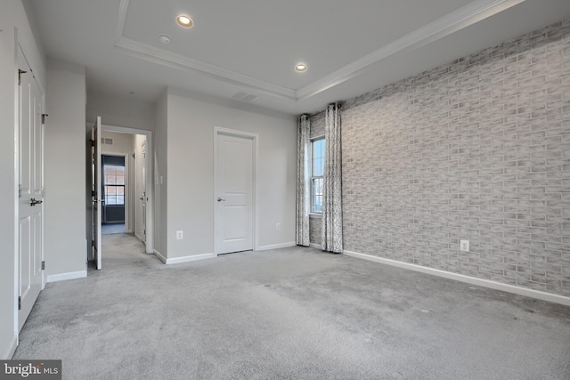 unfurnished bedroom with baseboards, brick wall, a raised ceiling, and light colored carpet