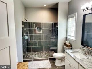 bathroom with a tile shower, vanity, and toilet