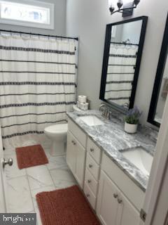 bathroom with double vanity, curtained shower, toilet, and a sink