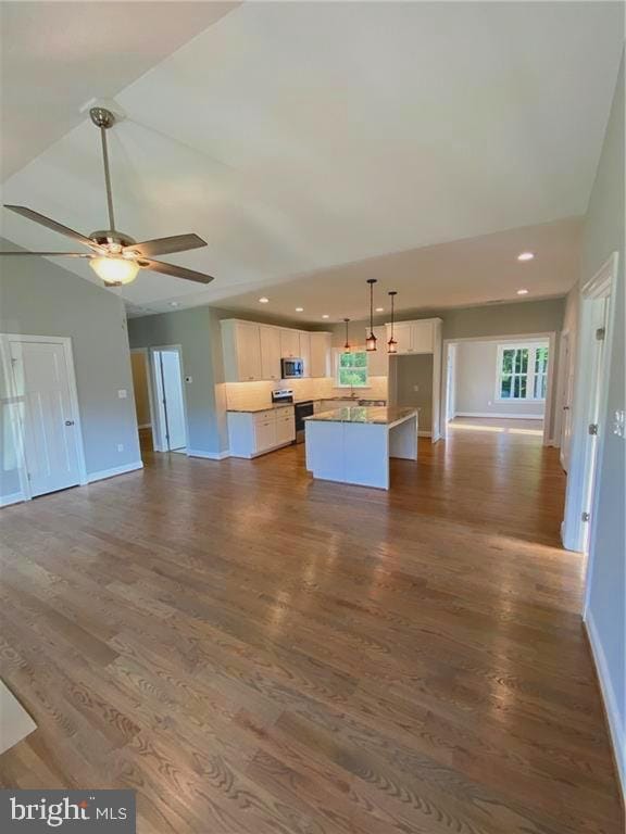 kitchen featuring white cabinets, a kitchen island, stainless steel microwave, and open floor plan