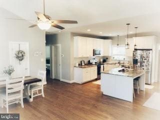 kitchen featuring wood finished floors, white cabinets, hanging light fixtures, appliances with stainless steel finishes, and a kitchen bar