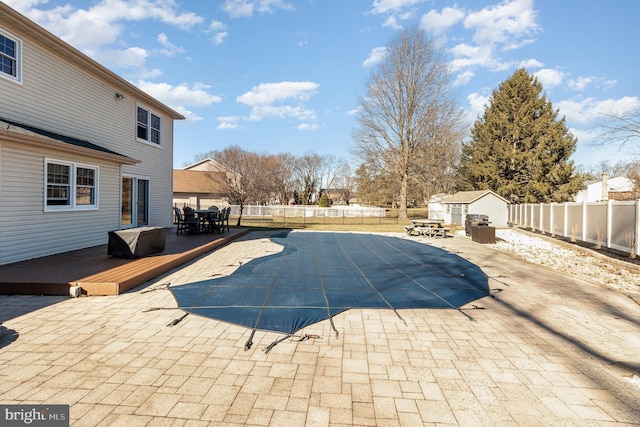 view of swimming pool featuring a deck, outdoor dining area, a fenced backyard, and a storage unit