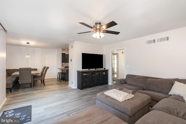 living area with light wood finished floors, visible vents, baseboards, and a ceiling fan