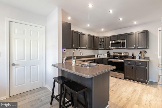 kitchen with a breakfast bar, appliances with stainless steel finishes, a peninsula, light wood-style floors, and a sink