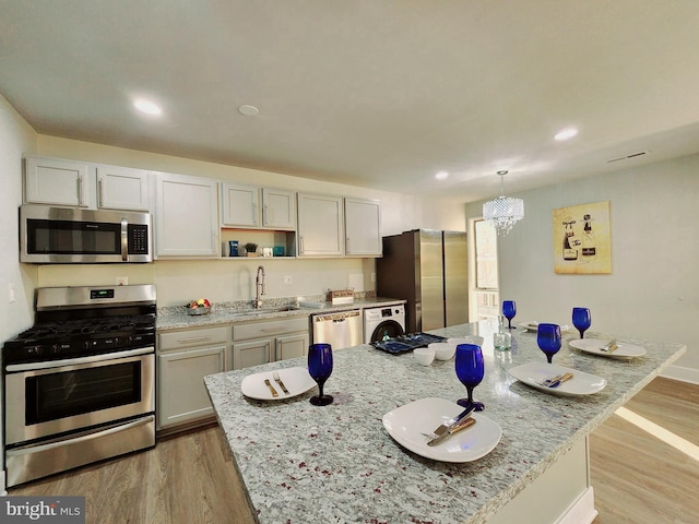 kitchen featuring a kitchen island, appliances with stainless steel finishes, light stone countertops, light wood-type flooring, and a sink