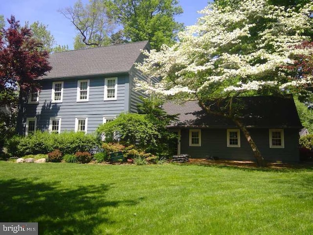 rear view of house featuring a yard and roof with shingles