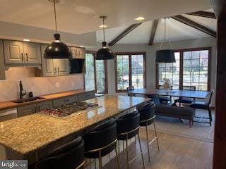 kitchen featuring beam ceiling, a sink, a kitchen island, stainless steel gas stovetop, and light stone countertops