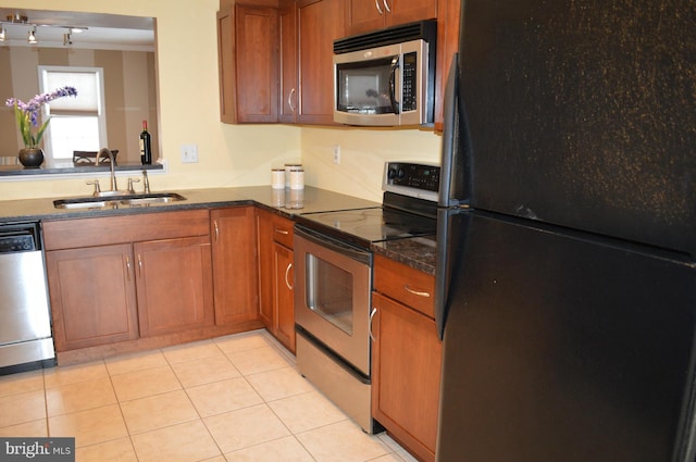 kitchen with brown cabinets, light tile patterned floors, stainless steel appliances, dark countertops, and a sink