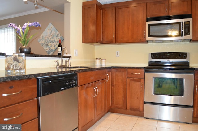 kitchen featuring light tile patterned floors, dark stone counters, ornamental molding, stainless steel appliances, and a sink