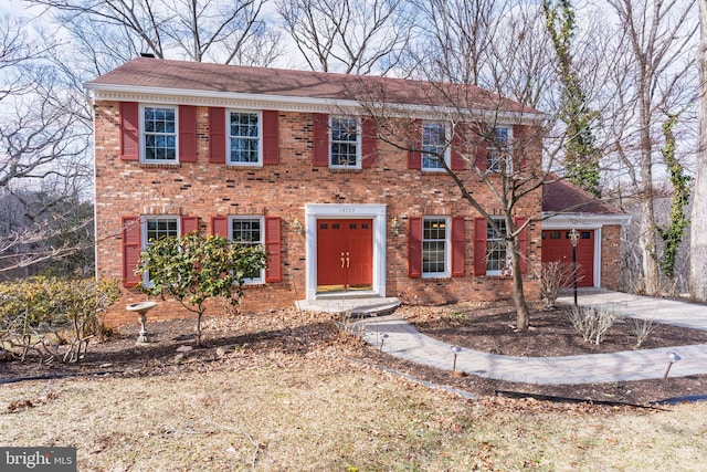 colonial home with driveway, brick siding, and an attached garage