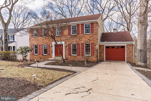 colonial-style house featuring concrete driveway, brick siding, a chimney, and an attached garage