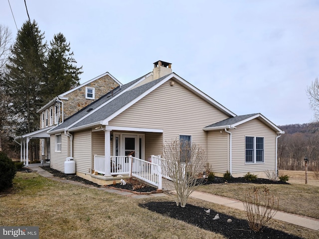 view of front of house featuring roof with shingles, a chimney, and a front yard