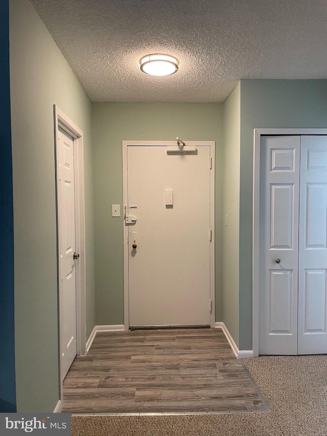 doorway to outside featuring a textured ceiling, wood finished floors, and baseboards