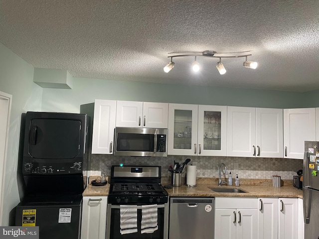 kitchen with stainless steel appliances, stacked washer and clothes dryer, white cabinets, and a sink