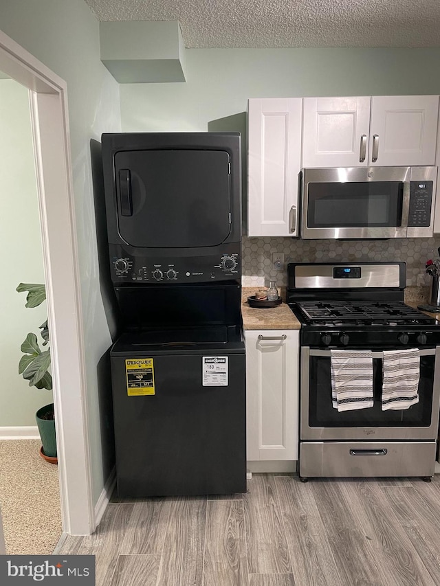 kitchen featuring white cabinets, stacked washer and clothes dryer, light wood-style flooring, appliances with stainless steel finishes, and a textured ceiling