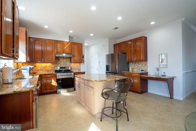 kitchen featuring under cabinet range hood, appliances with stainless steel finishes, light stone counters, and a center island