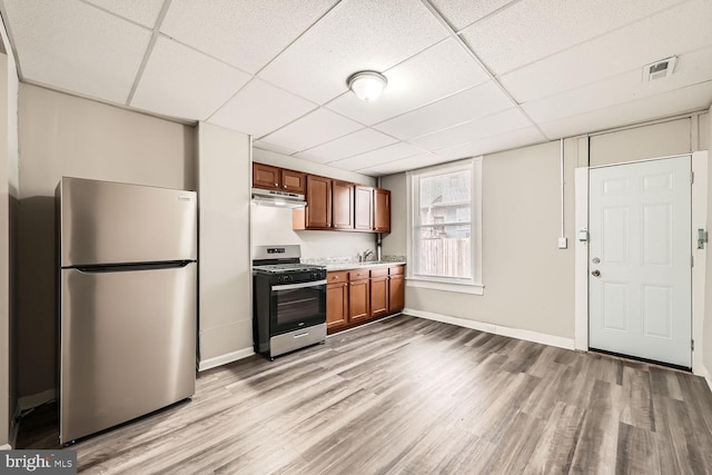 kitchen with light wood-style flooring, under cabinet range hood, light countertops, appliances with stainless steel finishes, and brown cabinets