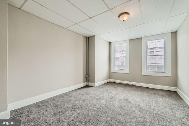 empty room with carpet floors, a paneled ceiling, and baseboards